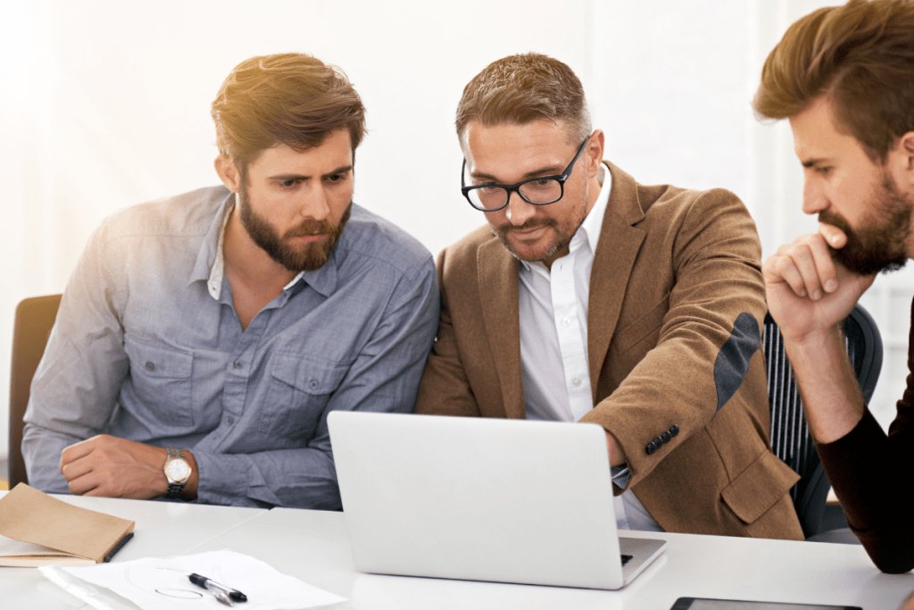 Three businessmen looking at a laptop in an office.