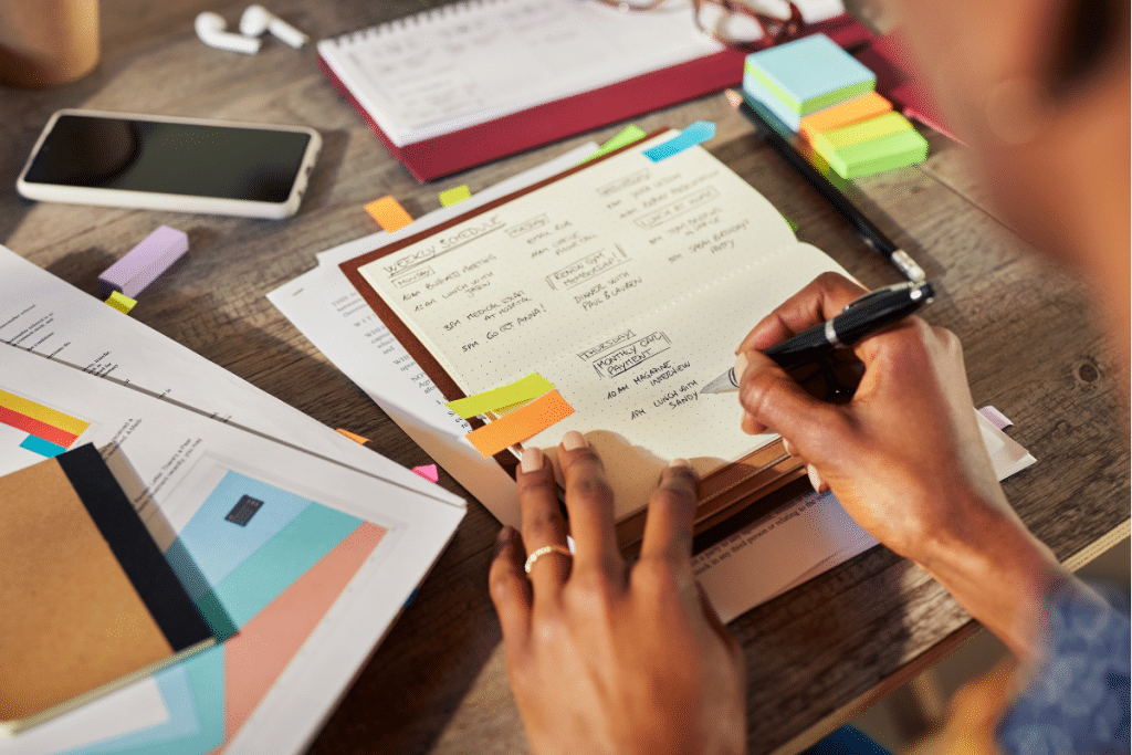 A woman is writing on a notebook at a desk.