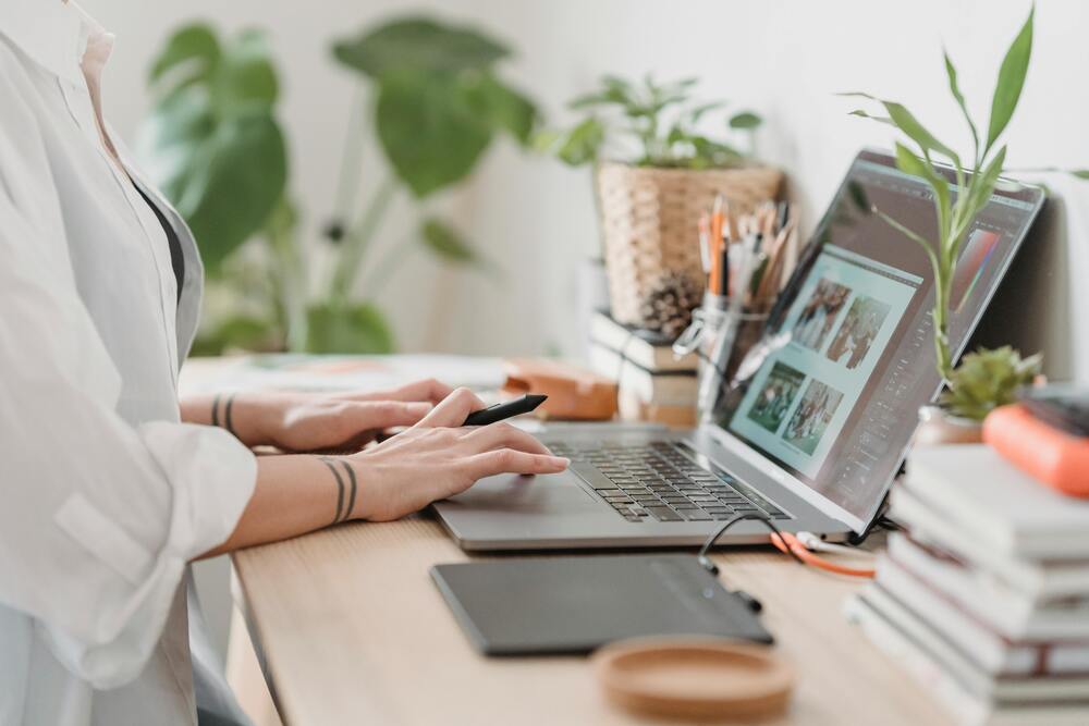 Person working on a creative design project at a modern workstation with a laptop and various plants.