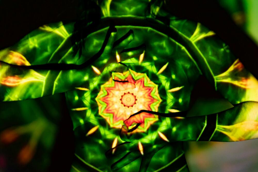 Vivid green and yellow kaleidoscopic pattern projected onto a person's back and hands.