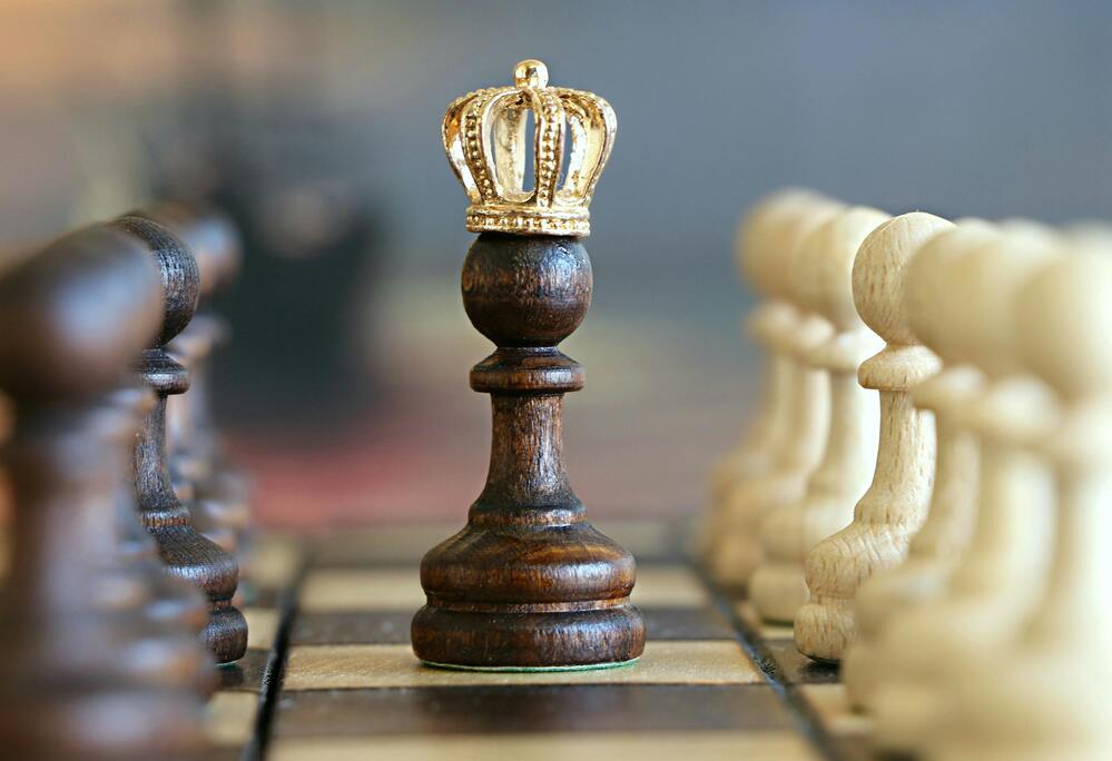 Chess pawn with a crown surrounded by white chess pieces