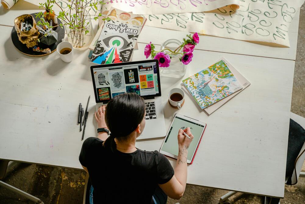 Designer working on graphics at a creative workstation, surrounded by colorful art supplies and inspirational posters.