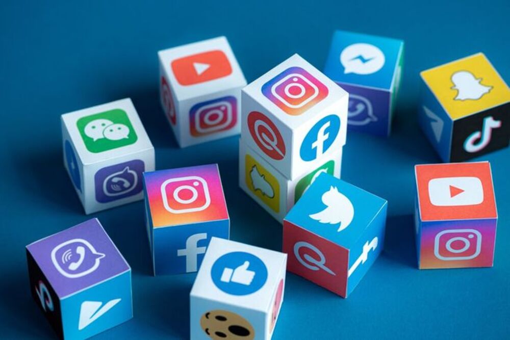 Colorful social media logo cubes on a blue background, featuring Instagram, Facebook, Twitter, and more iconic platforms.